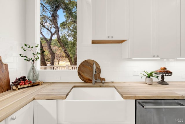 interior details featuring sink, wood counters, tasteful backsplash, stainless steel dishwasher, and white cabinets