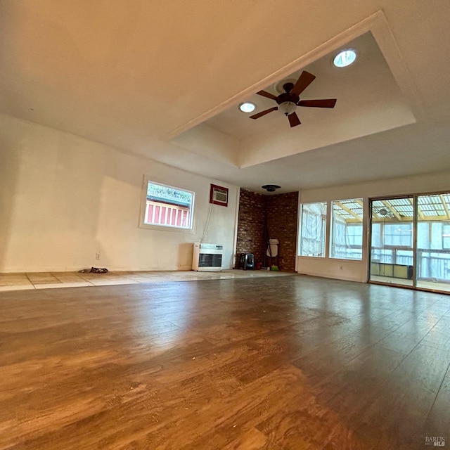 unfurnished living room with a tray ceiling, ceiling fan, heating unit, and hardwood / wood-style flooring