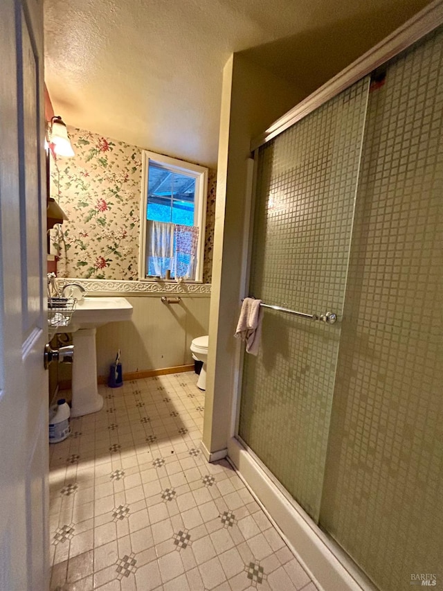 bathroom with a textured ceiling, toilet, and a shower with door