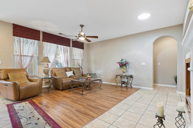 living room with arched walkways, ceiling fan, visible vents, baseboards, and light wood-style floors