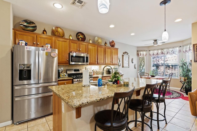 kitchen featuring a kitchen island with sink, ceiling fan, light tile patterned floors, decorative light fixtures, and stainless steel appliances