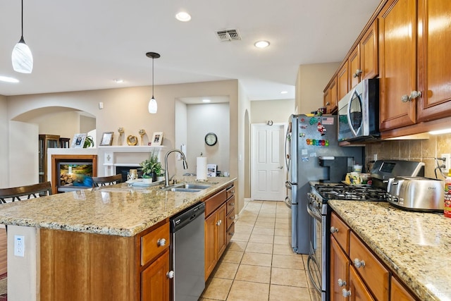 kitchen featuring brown cabinets, visible vents, appliances with stainless steel finishes, a sink, and a lit fireplace