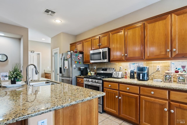 kitchen with a sink, visible vents, appliances with stainless steel finishes, tasteful backsplash, and brown cabinetry