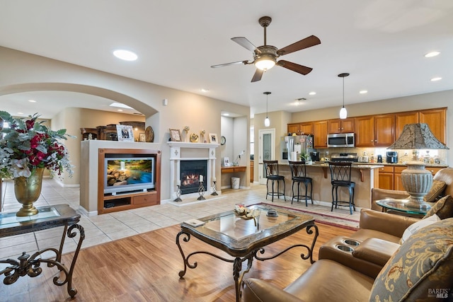 living area with light tile patterned floors, baseboards, a ceiling fan, a lit fireplace, and recessed lighting