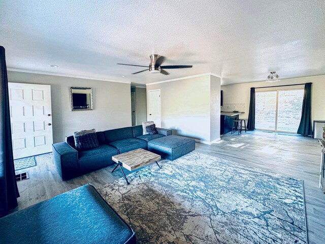 living room featuring ceiling fan, crown molding, wood-type flooring, and a textured ceiling