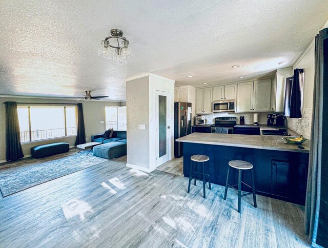 kitchen featuring a textured ceiling, kitchen peninsula, a kitchen breakfast bar, stainless steel appliances, and light hardwood / wood-style flooring