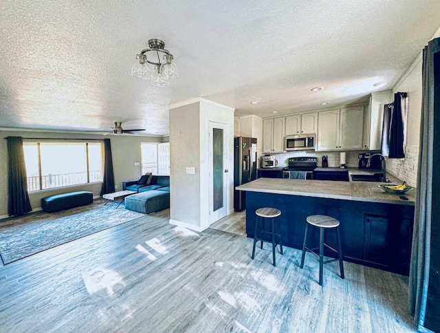 kitchen featuring stainless steel appliances, open floor plan, light wood-type flooring, a peninsula, and a kitchen bar