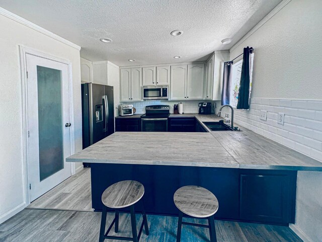 kitchen with sink, kitchen peninsula, stainless steel appliances, white cabinets, and a breakfast bar