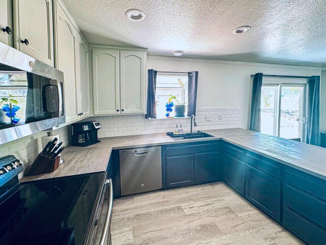 kitchen with backsplash, a textured ceiling, light hardwood / wood-style flooring, sink, and stainless steel appliances