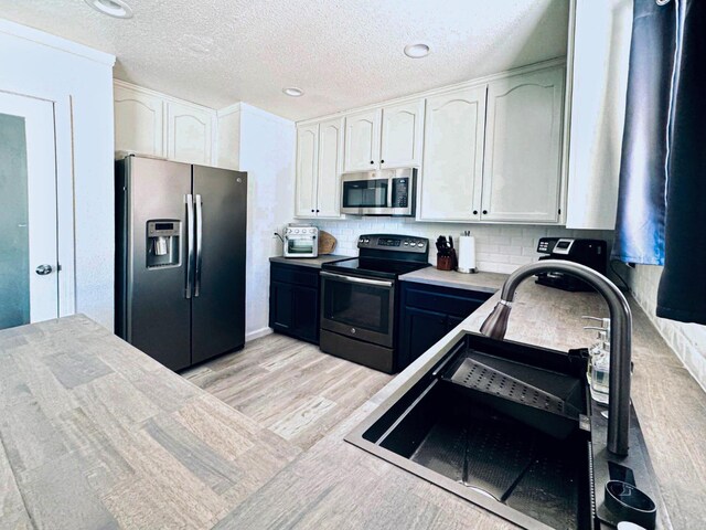 kitchen featuring appliances with stainless steel finishes, sink, white cabinetry, decorative backsplash, and light hardwood / wood-style flooring