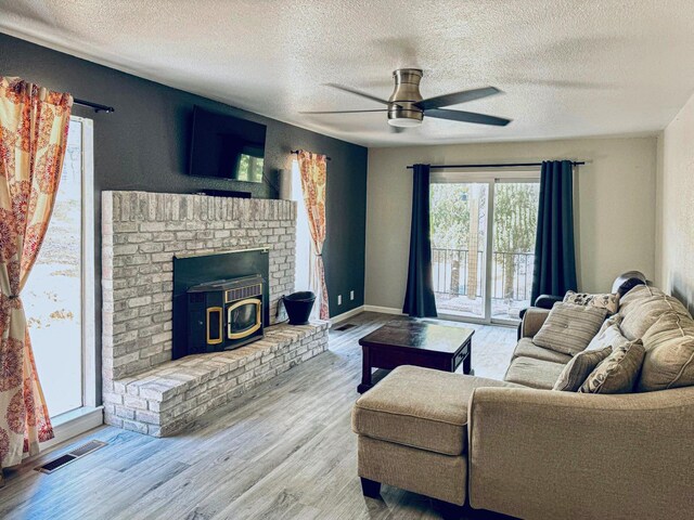 living room featuring light hardwood / wood-style floors, a wood stove, a textured ceiling, and ceiling fan