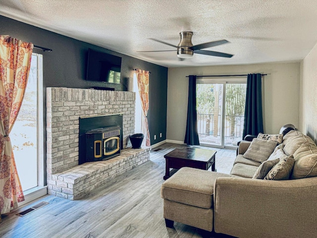 living room with baseboards, visible vents, ceiling fan, wood finished floors, and a wood stove