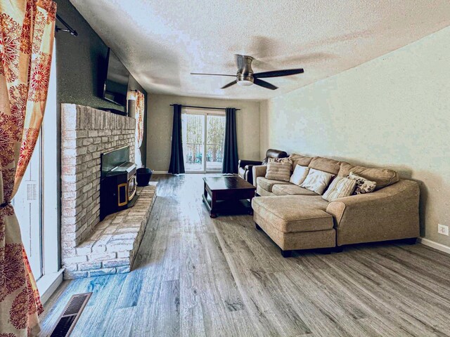 living room with ceiling fan, a wood stove, a textured ceiling, and hardwood / wood-style floors