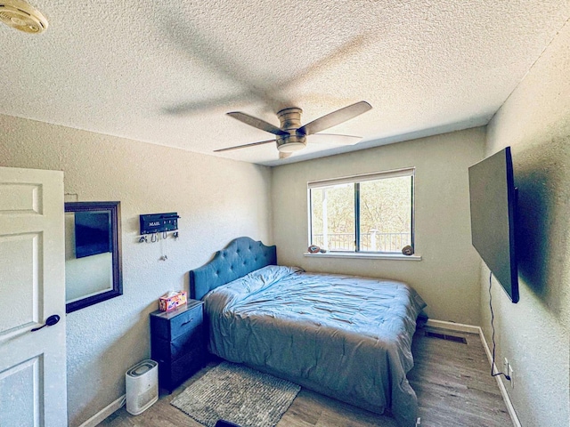 bedroom with a textured ceiling, wood-type flooring, and ceiling fan