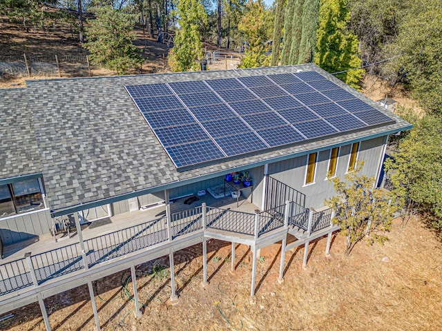 exterior space with a shingled roof, a deck, and solar panels