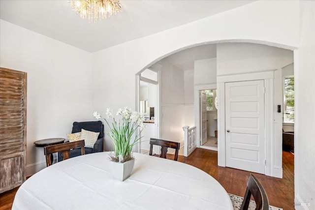 dining space with arched walkways, a notable chandelier, and dark wood finished floors