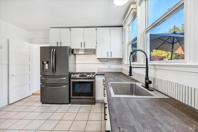 kitchen featuring dark countertops, appliances with stainless steel finishes, under cabinet range hood, white cabinetry, and a sink