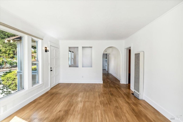 empty room featuring light wood-type flooring, baseboards, arched walkways, and a heating unit