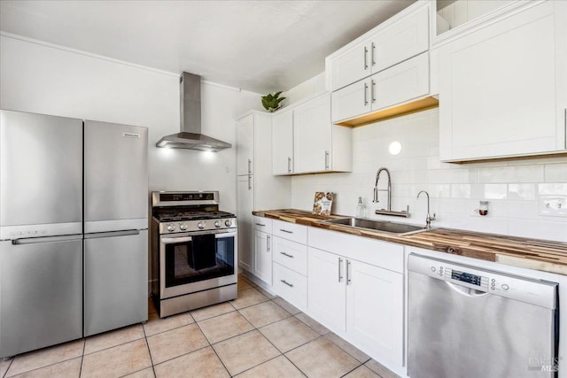 kitchen with tasteful backsplash, appliances with stainless steel finishes, a sink, wall chimney range hood, and butcher block countertops