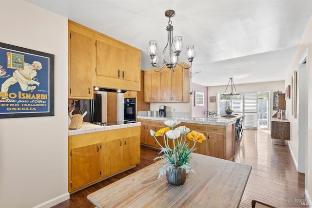 kitchen with kitchen peninsula, black appliances, decorative light fixtures, tile countertops, and a kitchen island