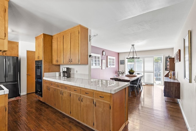 kitchen with hanging light fixtures, double oven, fridge, tile counters, and kitchen peninsula