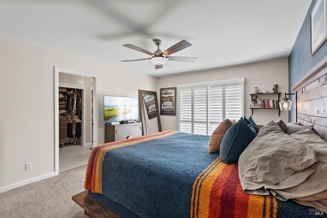 carpeted bedroom featuring a walk in closet and ceiling fan