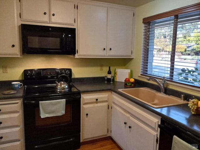 kitchen featuring white cabinets, dark countertops, a sink, and black appliances