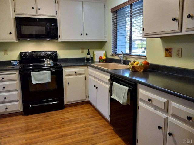 kitchen featuring dark countertops, a sink, black appliances, light wood-style flooring, and white cabinetry