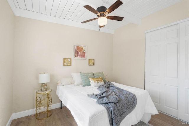 bedroom featuring beamed ceiling, hardwood / wood-style flooring, ceiling fan, and a closet