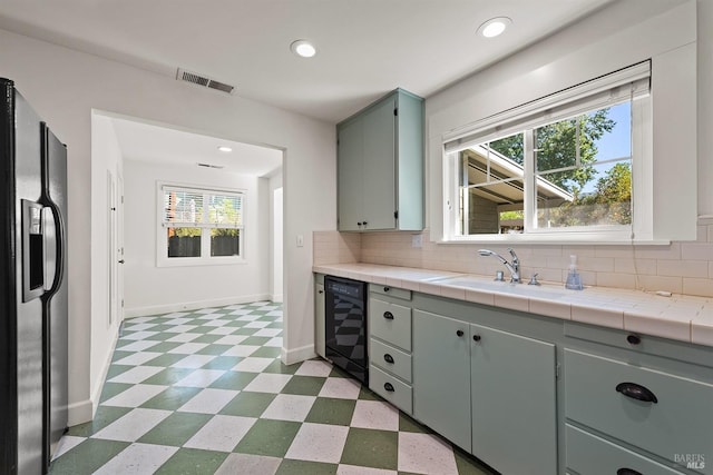 kitchen with beverage cooler, black fridge with ice dispenser, tile countertops, and plenty of natural light