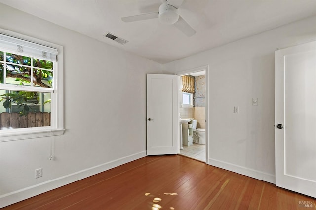 unfurnished bedroom featuring multiple windows, hardwood / wood-style floors, ceiling fan, and ensuite bath