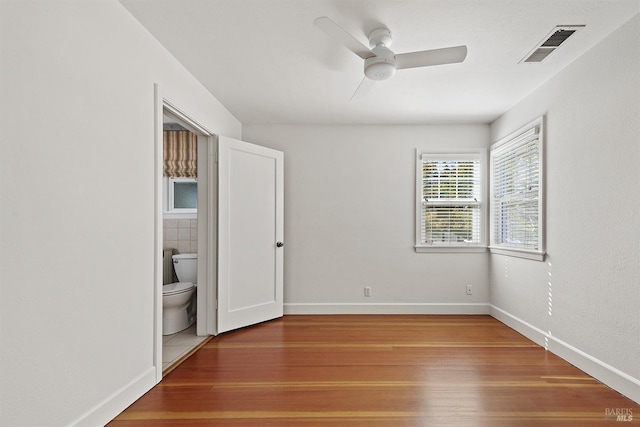 unfurnished bedroom featuring ensuite bath, ceiling fan, and hardwood / wood-style flooring