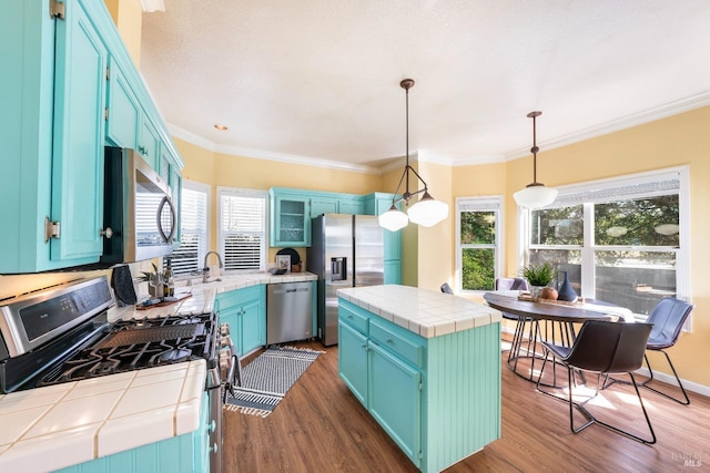 kitchen with ornamental molding, stainless steel appliances, tile counters, dark wood-type flooring, and blue cabinets