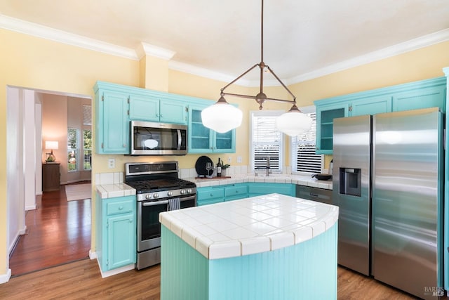 kitchen with appliances with stainless steel finishes, wood finished floors, blue cabinets, and tile counters