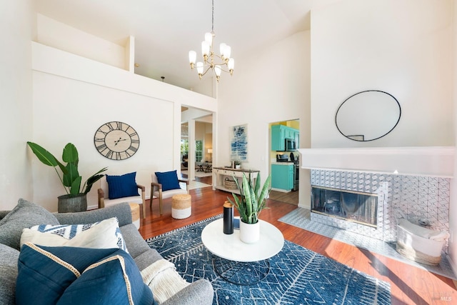 living room featuring a notable chandelier, a fireplace, a high ceiling, and wood finished floors