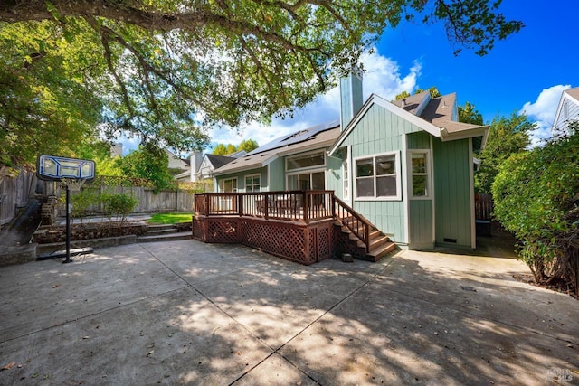 back of house featuring roof mounted solar panels, a wooden deck, fence private yard, a chimney, and a patio area