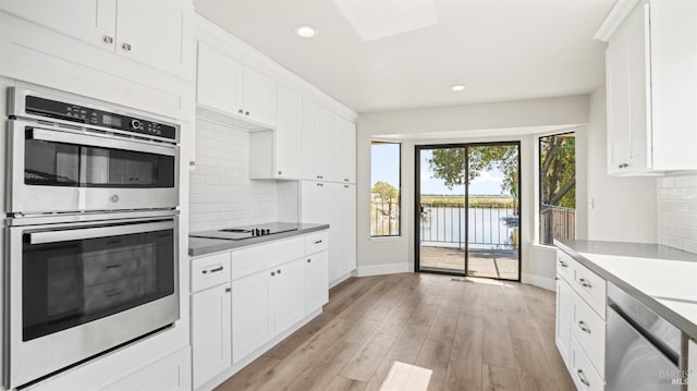 kitchen featuring tasteful backsplash, white cabinets, light hardwood / wood-style flooring, stainless steel appliances, and a water view