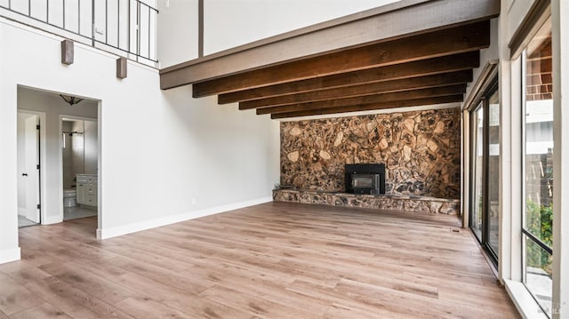 unfurnished living room featuring a wood stove, beam ceiling, and light hardwood / wood-style floors