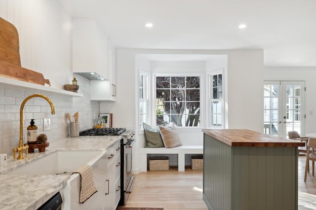 kitchen featuring wooden counters, french doors, stainless steel range with gas cooktop, white cabinets, and tasteful backsplash