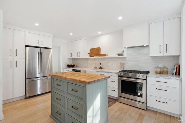 kitchen with wooden counters, stainless steel appliances, a kitchen island, white cabinetry, and backsplash