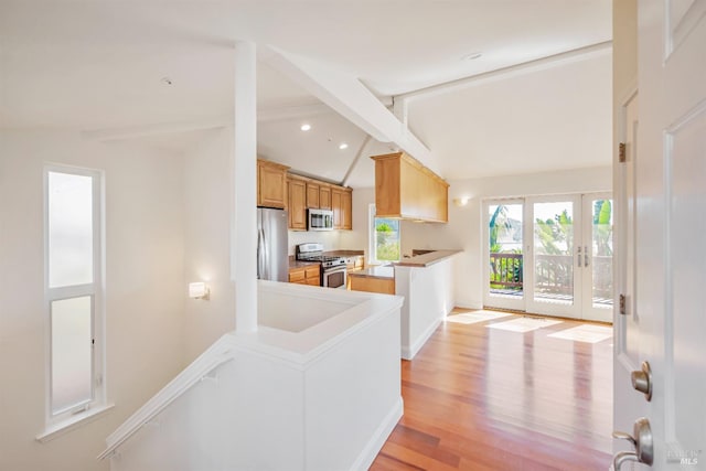 kitchen with lofted ceiling with beams, light hardwood / wood-style floors, stainless steel appliances, light brown cabinetry, and french doors