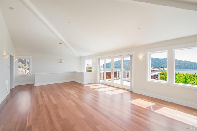 unfurnished living room featuring lofted ceiling with beams, a wealth of natural light, a mountain view, and light wood-type flooring