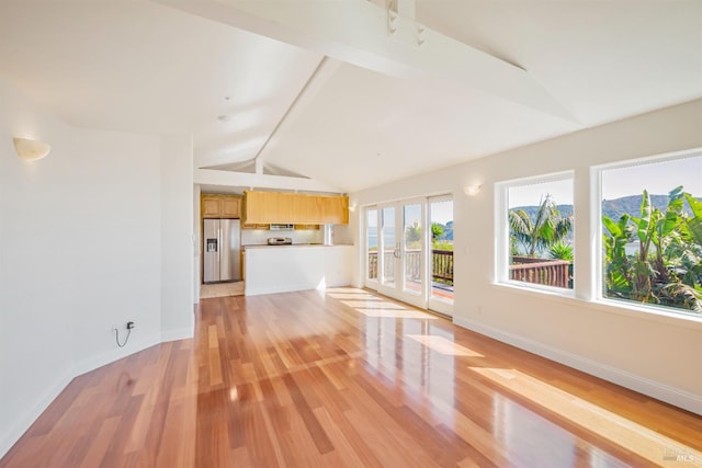 unfurnished living room featuring lofted ceiling with beams, a wealth of natural light, and light hardwood / wood-style flooring