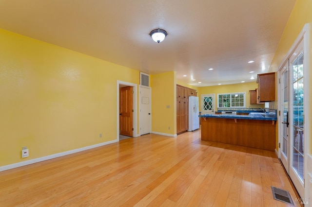 kitchen with white refrigerator with ice dispenser, light hardwood / wood-style floors, and kitchen peninsula