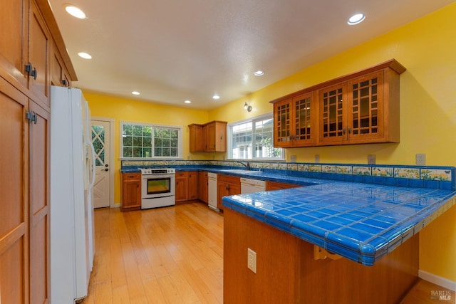 kitchen featuring sink, tile counters, kitchen peninsula, white appliances, and light hardwood / wood-style floors