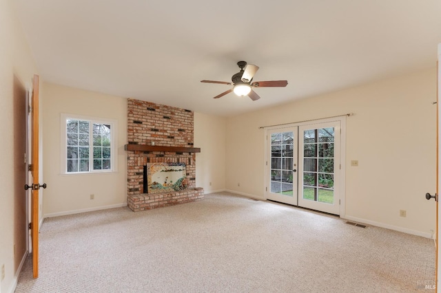 unfurnished living room featuring a brick fireplace, light carpet, ceiling fan, and french doors