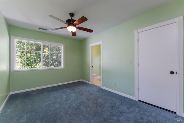 unfurnished bedroom with ceiling fan, ensuite bath, and dark carpet