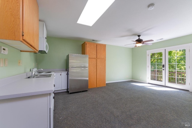 kitchen with sink, dark colored carpet, a skylight, stainless steel fridge, and ceiling fan