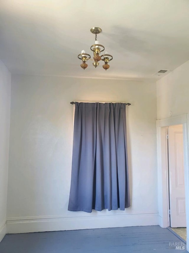 empty room featuring wood-type flooring and an inviting chandelier