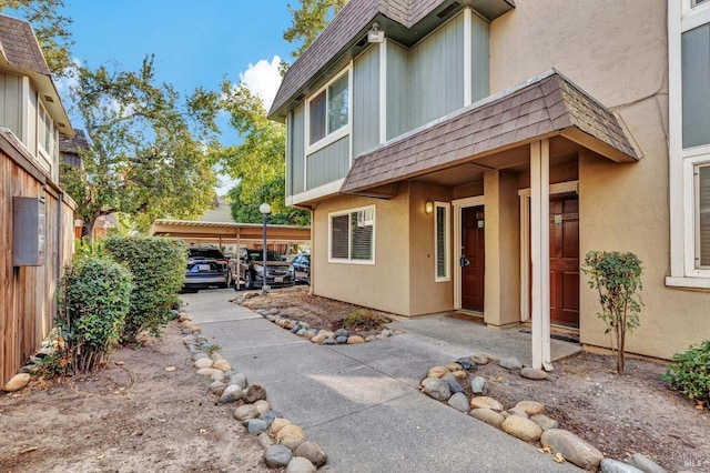 property entrance with a shingled roof, mansard roof, and stucco siding